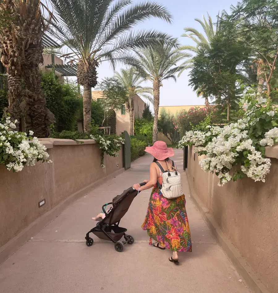 Luana pushing a stroller through a sunlit palm tree pathway  -  a quiet moment of motherhood in motion